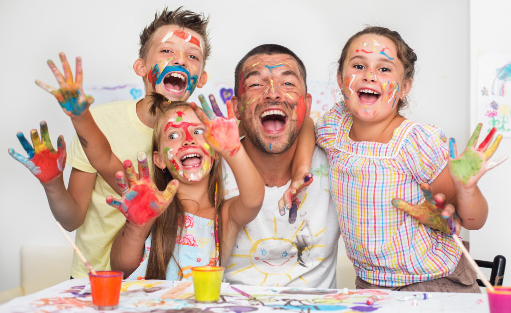 Father and young children with paint on their hands and faces